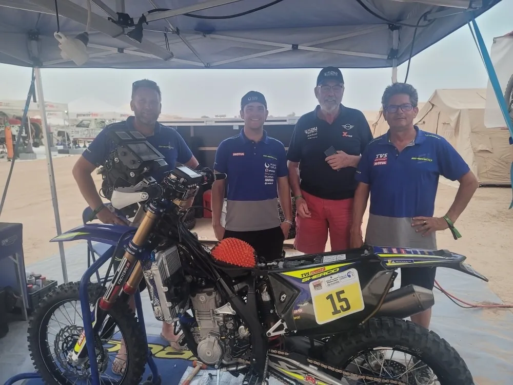 Motorcycle riders and their team gathered around a rally bike in the bivouac