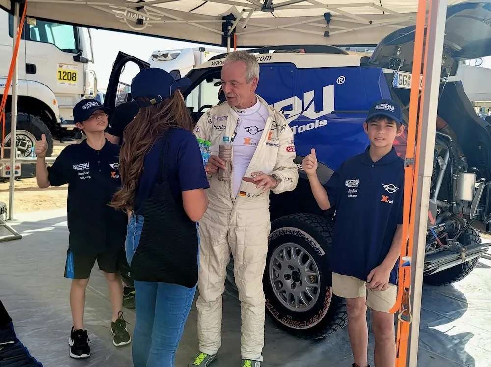 Stephan Schott in his racing suit with the children beside the blue SBVTools MINI